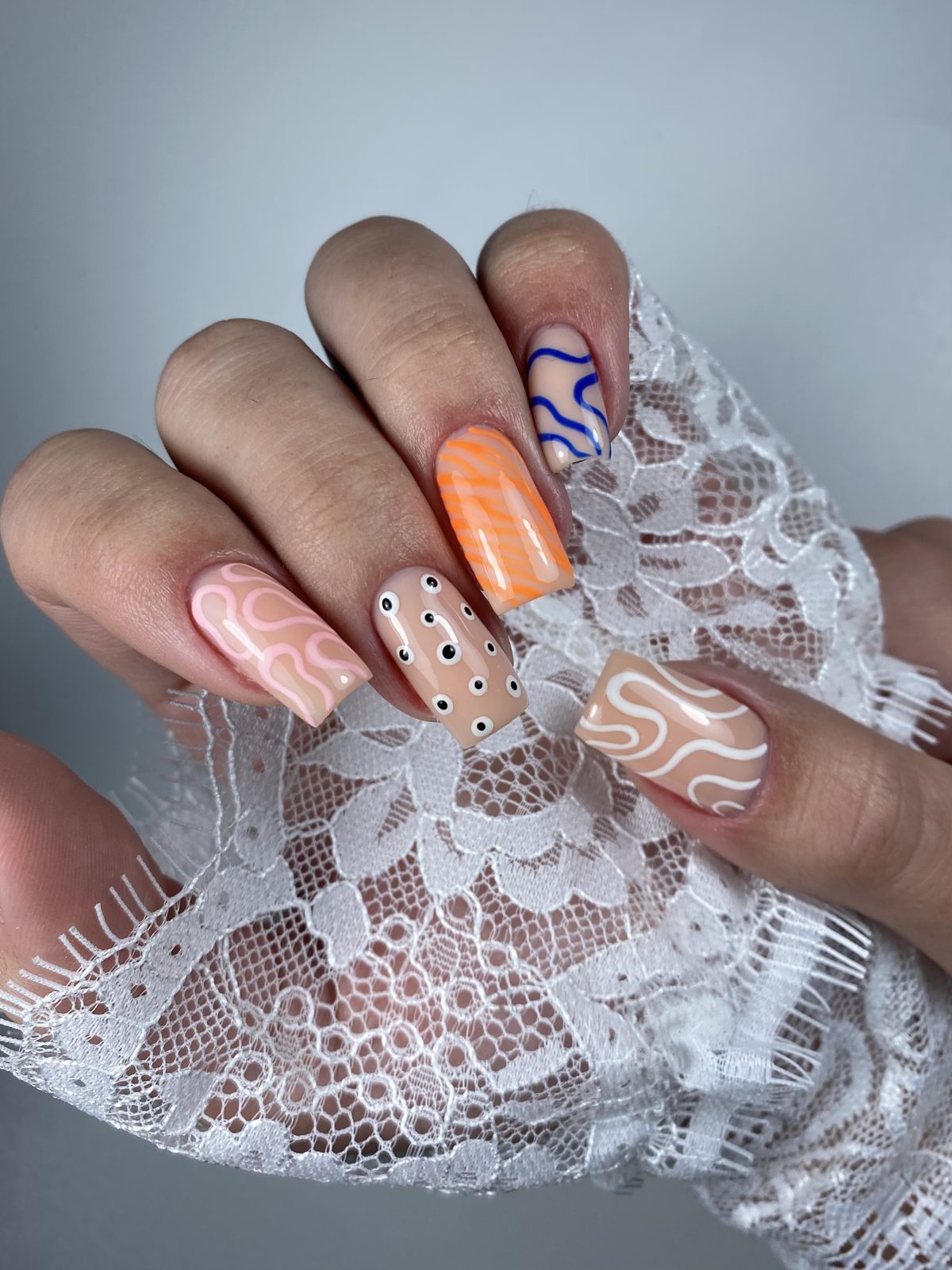 Speelse nail art met oranje, golflijnen en stippen op kant