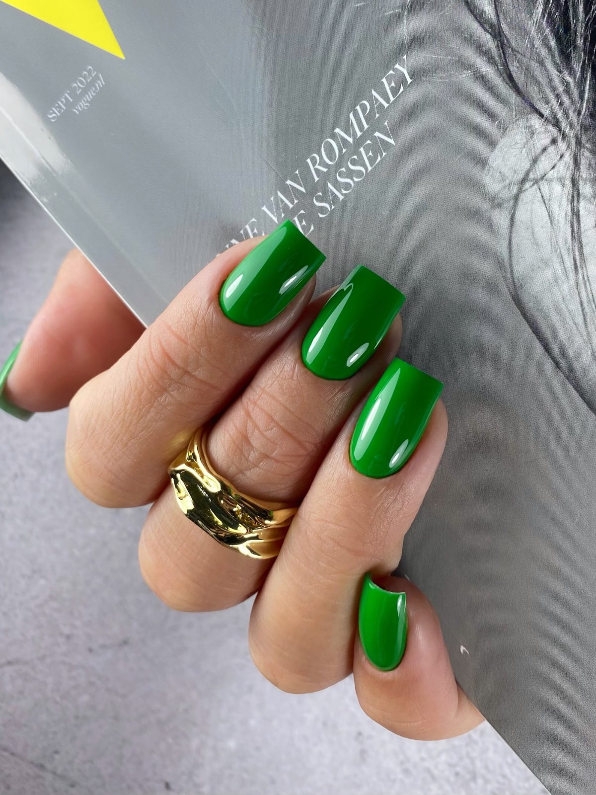 Glanzend groene nagels met een gouden ring, hand op een tijdschrift